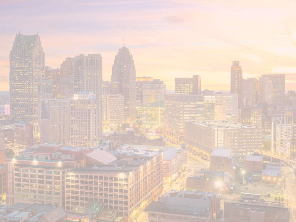 An aerial view of the Detroit cityscape with vibrant lights and a sunset in the sky behind it