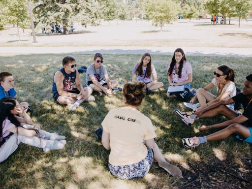 A group of youth sitting in a circle outside. 