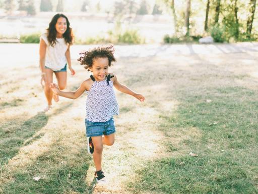 Woman playfully chasing after her young daughter in a park on a sunny day