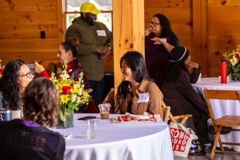 Several individuals gather in a dining room setting, talking and laughing with each other.