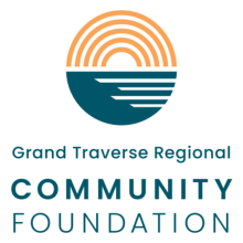 Logo for Grand Traverse Regional Community Foundation with a circle above the text that has two colors - green on the bottom half and orange on the top half. The orange appears to be the sun represented by an all orange rainbow shape and the land represented by the bottom half of the circle in dark green