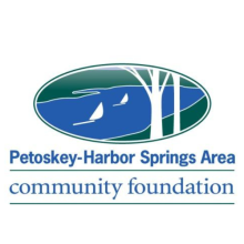 Logo for Petoskey Harbor Springs Area Community Foundation with the text below an oval that shows a picture of land and water meeting with sail boats in the water and trees that are to the right