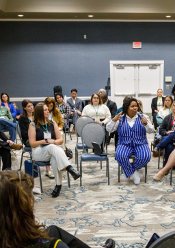 A woman attending a keynote at annual conference asks a question into the mic while others watch and listen intently 