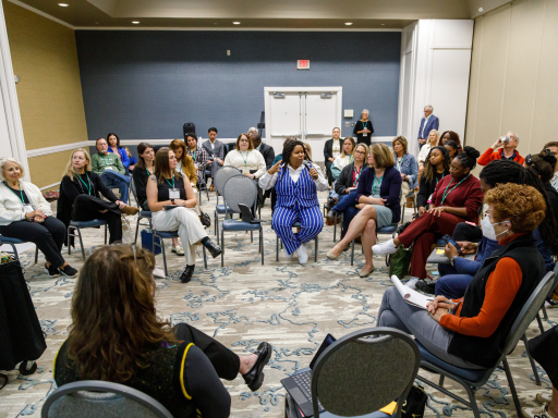 A woman attending a keynote at annual conference asks a question into the mic while others watch and listen intently 