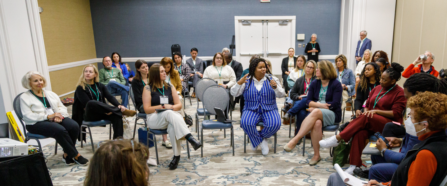A woman attending a keynote at annual conference asks a question into the mic while others watch and listen intently 