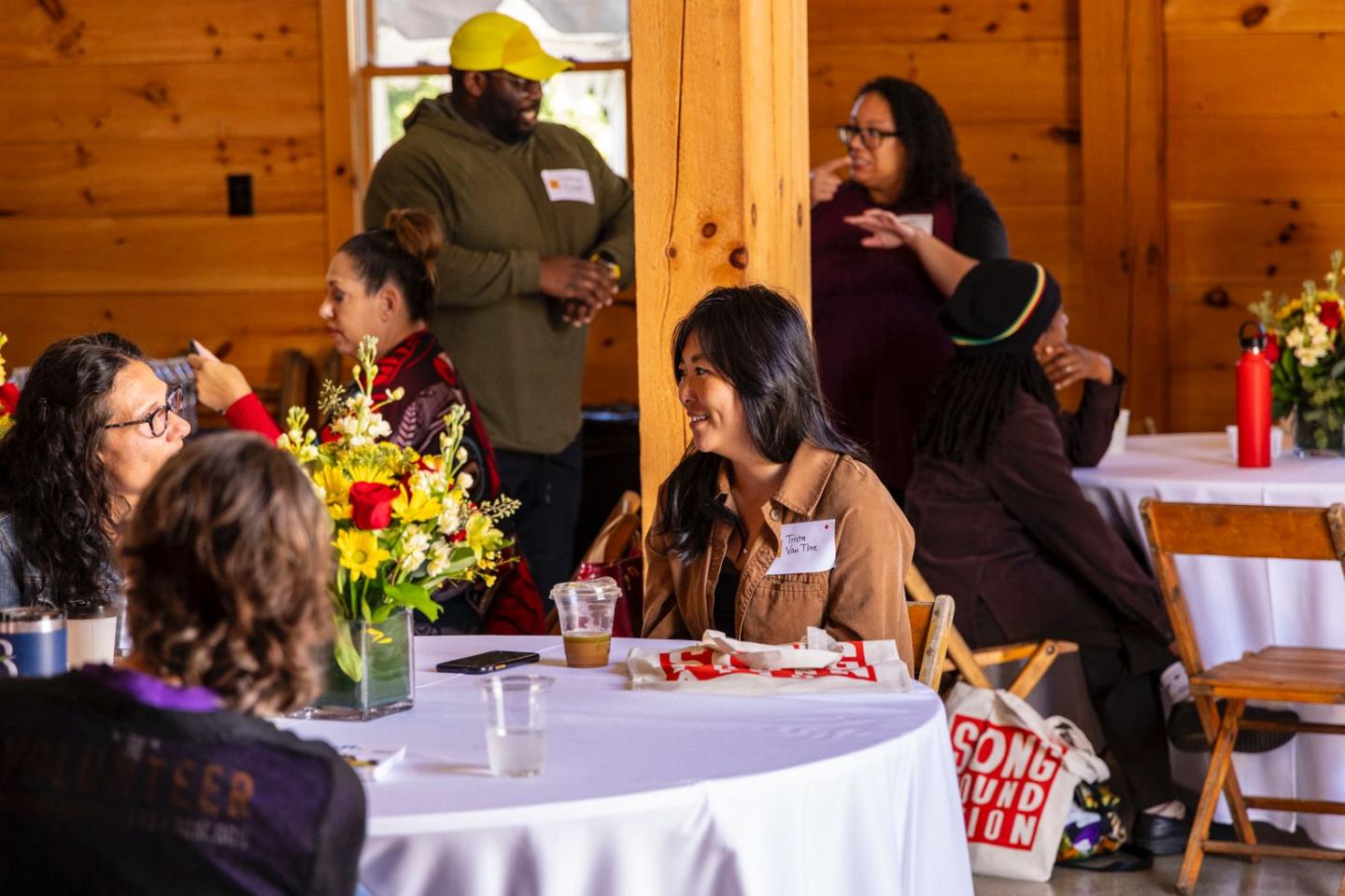 Several individuals gather in a dining room setting, talking and laughing with each other.