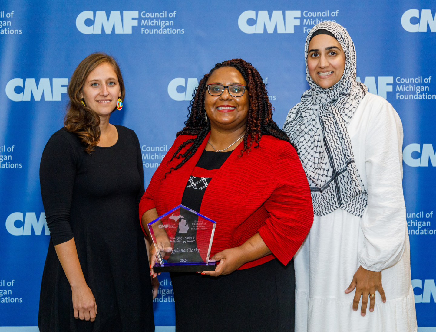 A photo of one of our award winners with the an EPIP Committee Chair person on either side of her standing in front of a branded photo backdrop