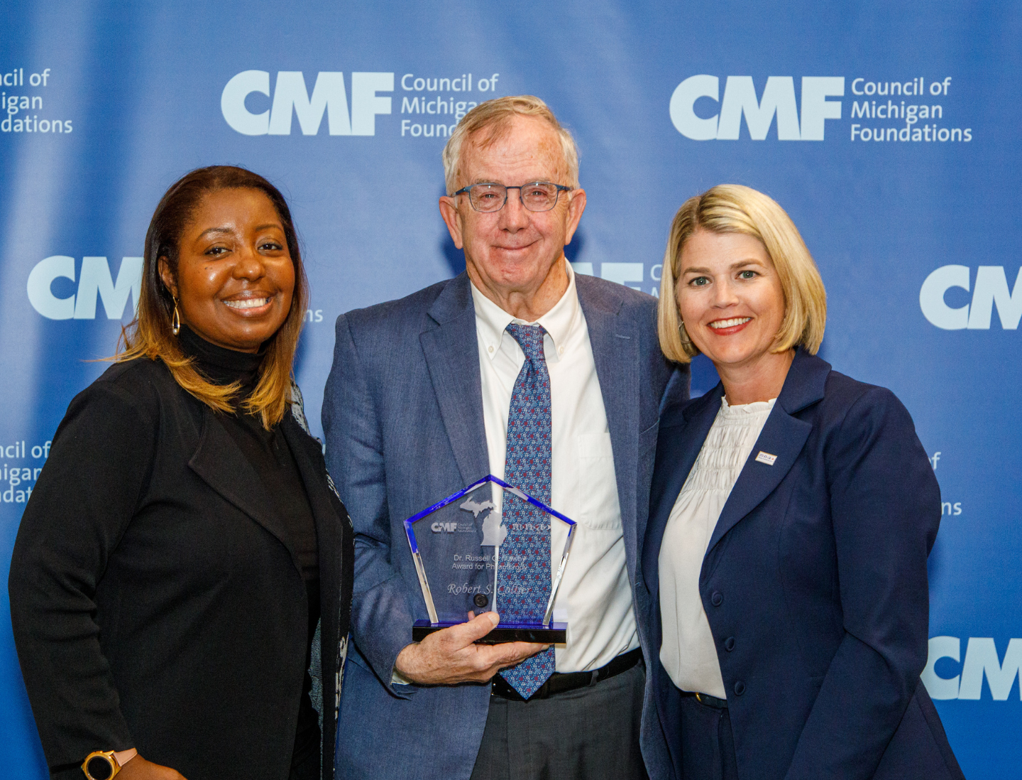 A photo of one of our award winners and two of the individuals who presented the award to him, all are standing in front of a CMF branded backdrop for a photo