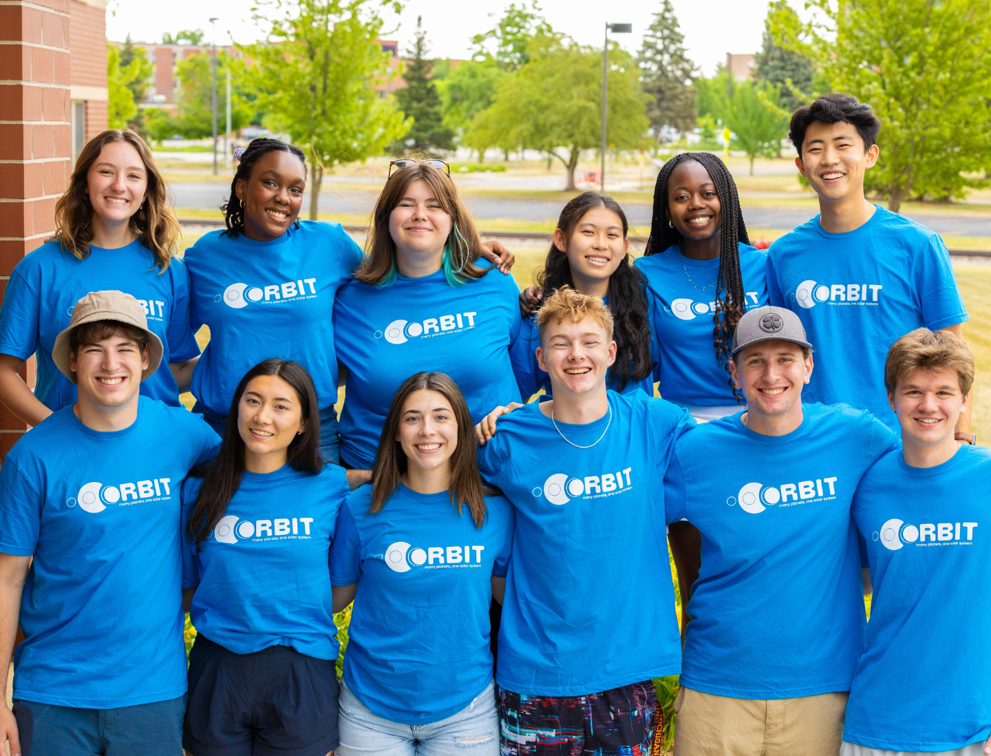 A group of youth stand outside in matching shirts and smiling at the camera