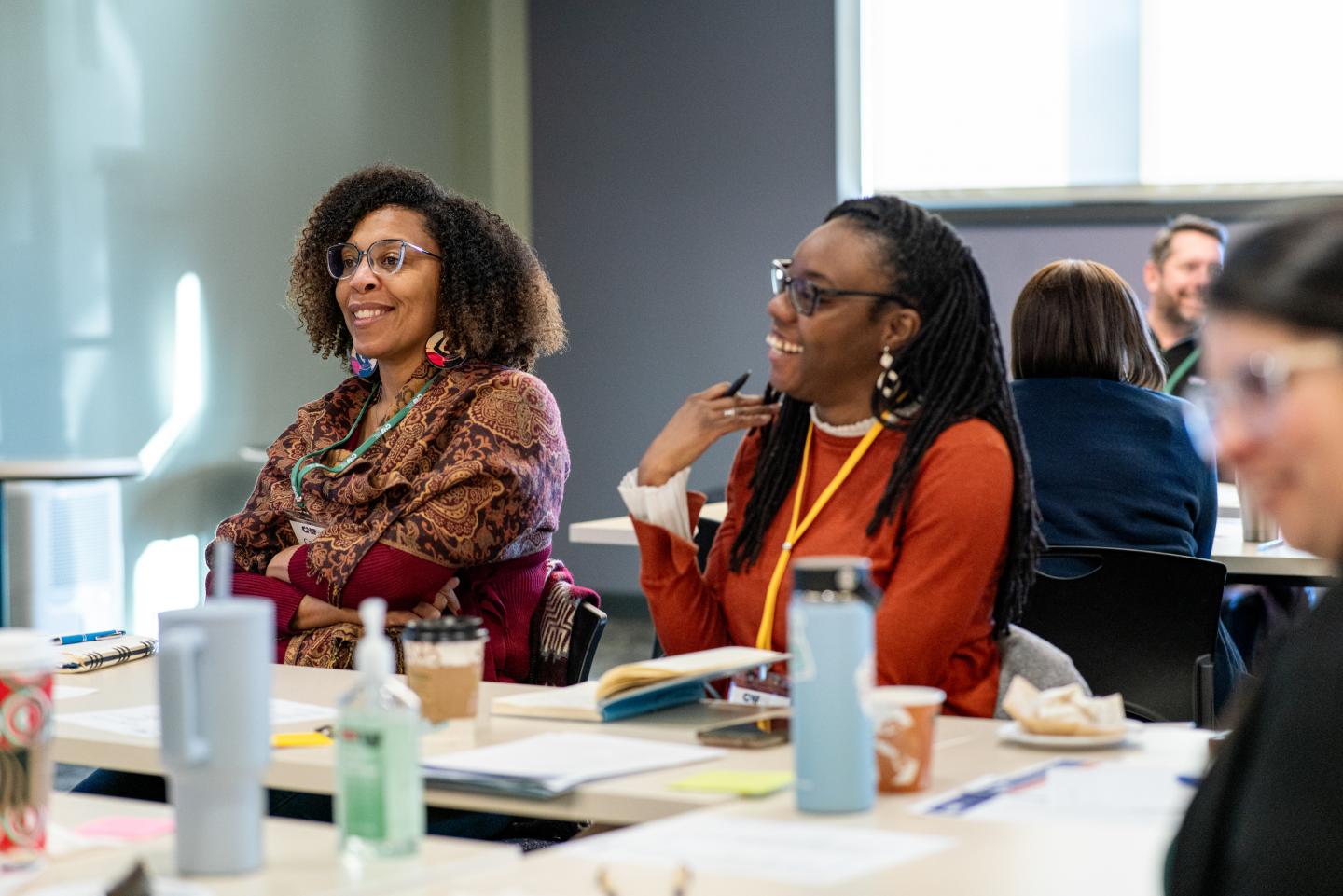 Two people, among a larger group, talking with a facilitator who is off screen.