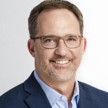 Headshot for Darin McKeever who is wearing a blue suit coat with lighter blue shirt and is wearing glasses and smiling at the camera