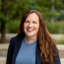 Headshot of Bridget McGuiggan, who is wearing a light blue sweater and a dark blue suit jacket, and smiling