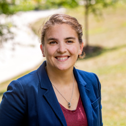 Headshot of Christine Stevens, wearing a maroon shirt and blue suit jacket, smiling