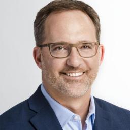 Headshot for Darin McKeever who is wearing a blue suit coat with lighter blue shirt and is wearing glasses and smiling at the camera