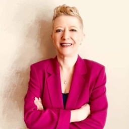 Headshot for Colleen Knight, facing the camera and smiling with her arms crossed, wearing a magenta suit jacket