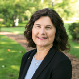 Headshot of Jenee Velasquez, smiling at the camera and wearing a light blue shirt under a dark suit jacket