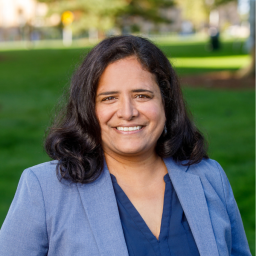 Headshot for Leena who is wearing a dark blue shirt under her light blue blazer and smiling at the camera