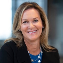 Headshot of Mary Culler in a black suit jacket and blue shirt smiling at the camera