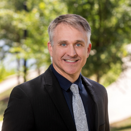 Headshot of Nathan Murphy, wearing a black suit jacket with a blue shirt and paisley patterned tie, smiling