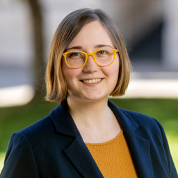 Headshot of Savanna Weber, wearing a mustard yellow shirt with a blue suit jacket, smiling at the camera