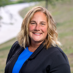 Headshot of Tammie TenBroeke, wearing a royal blue shirt under a dark blue suit jacket, smiling