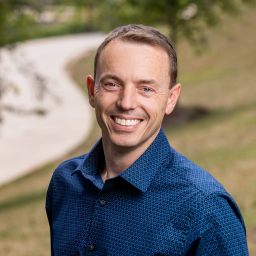 Headshot of Bill Corkill in a blue collared shirt, smiling